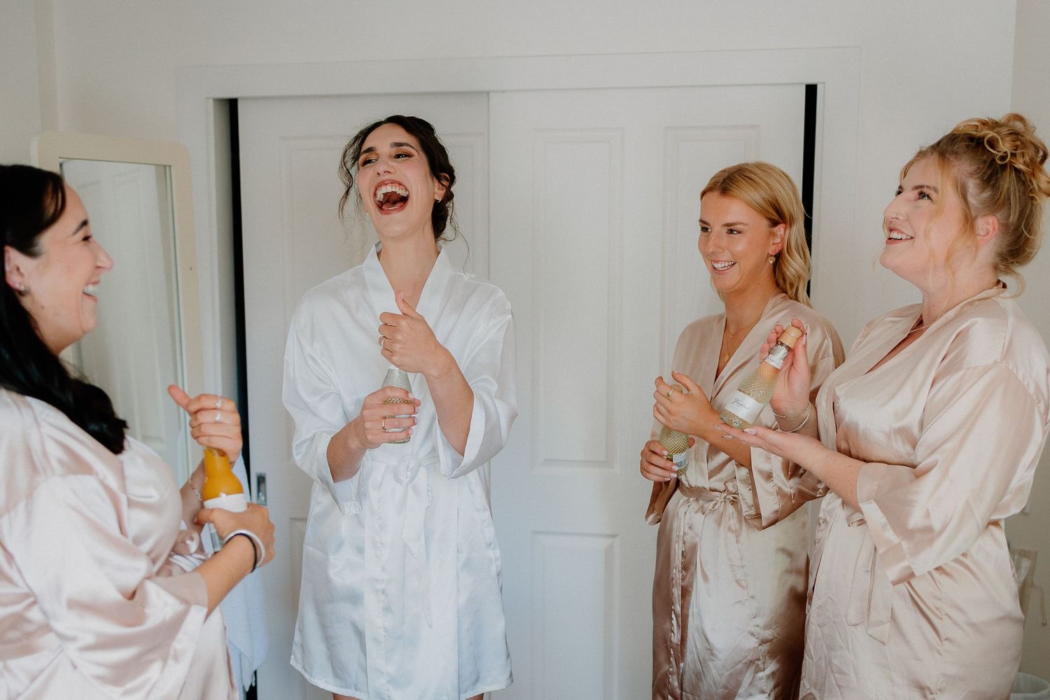 Two people getting ready in a bright white room, one wearing a silk robe and one in a delicate lace dress.
