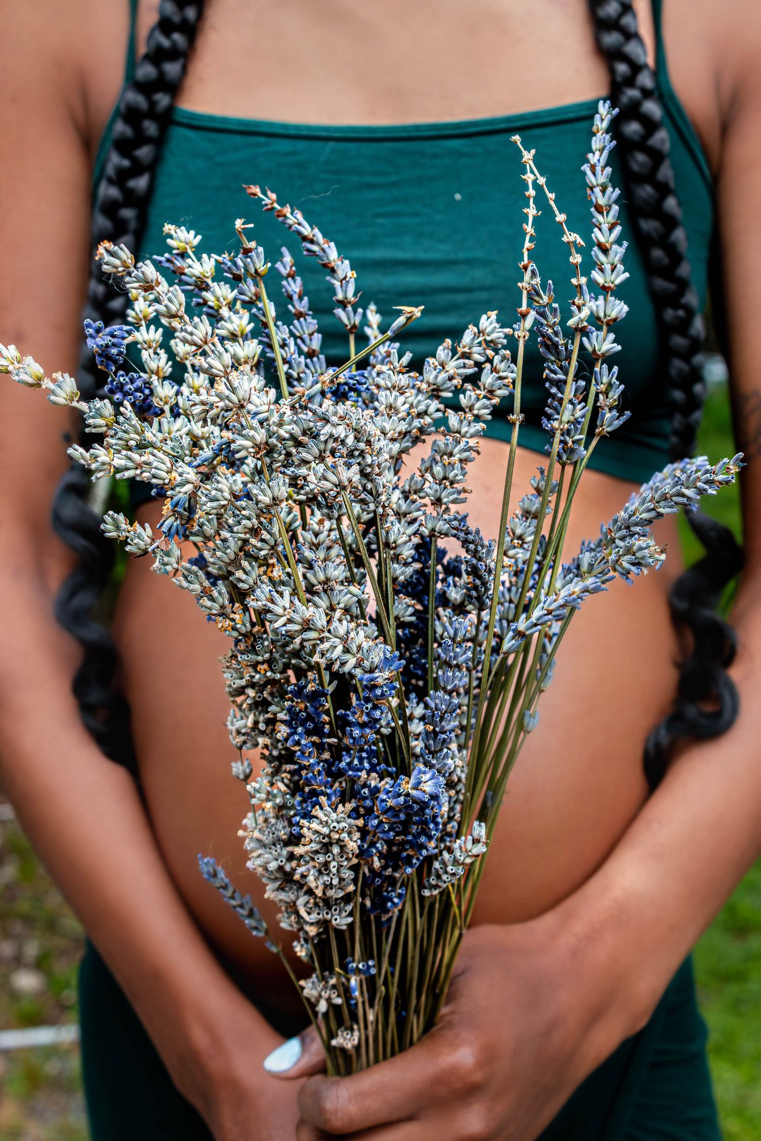 A bouquet of delicate dried white and blue flowers held against a teal green dress in summer sunlight.