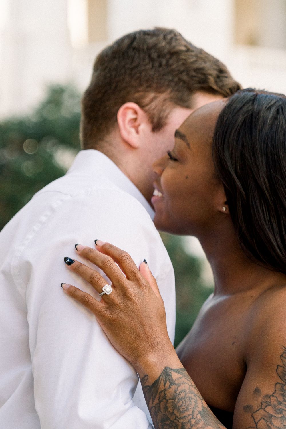 A loving couple shares an intimate moment as a diamond ring sparkles on her hand with visible tattoos.