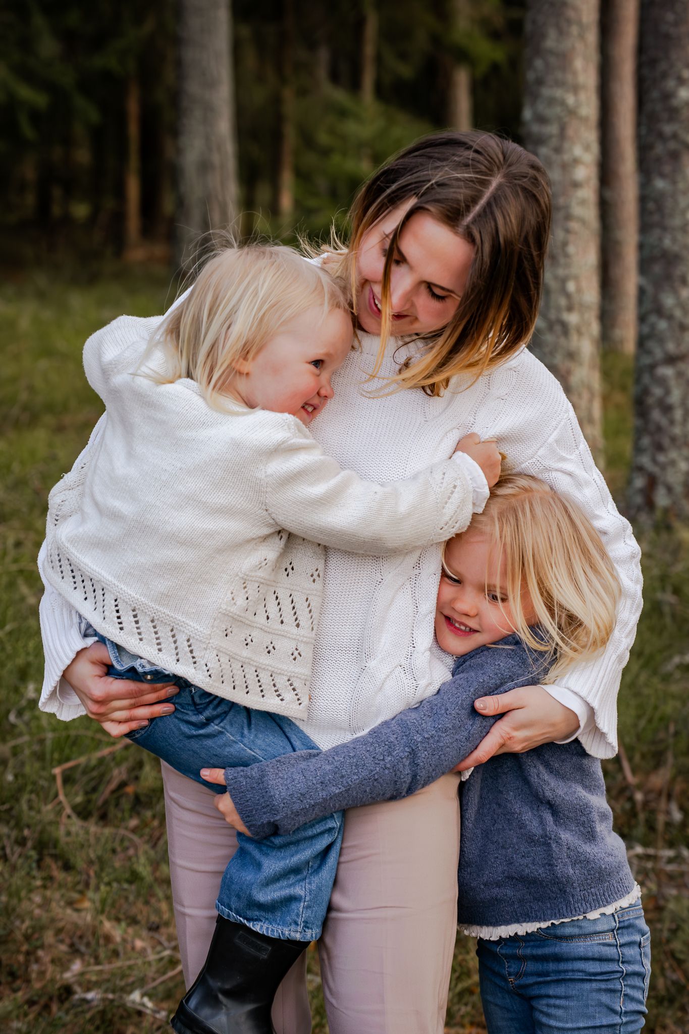 Kärleksfull bild från skogen på mamma som kramas om av dotter i famnen och en dotter vid höften. Fotograf, familjefotograf, Umeå