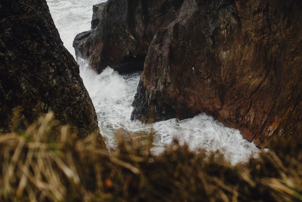 Dramatic rocky cliffs meet turbulent ocean waves crashing against the rugged coastline.