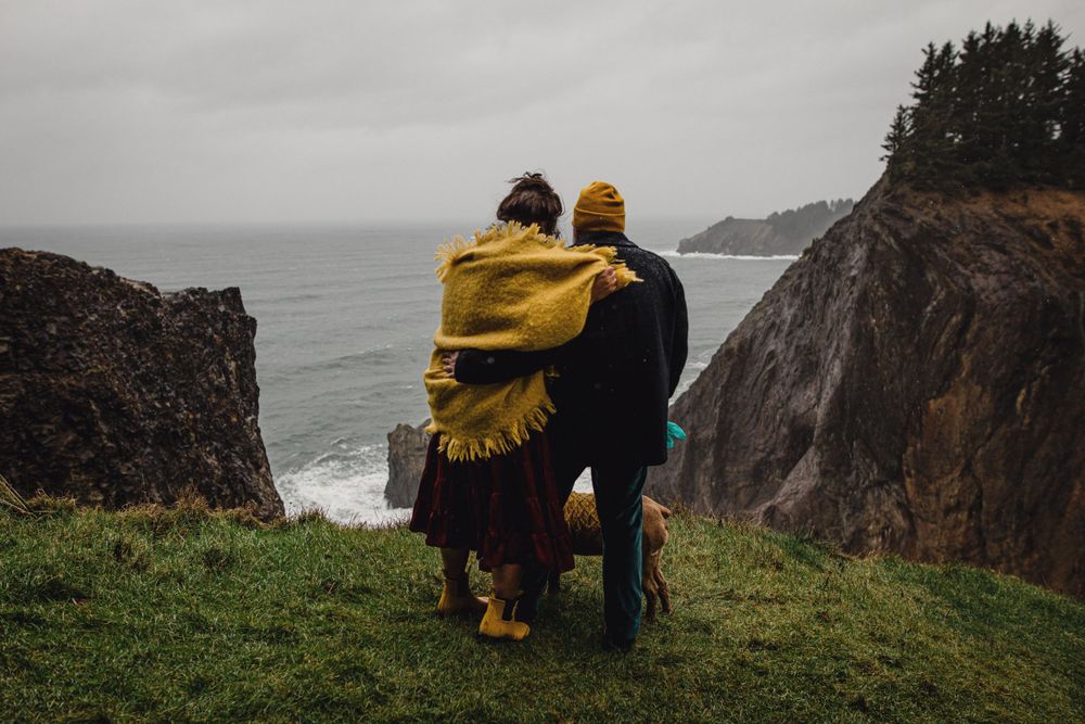 A couple in yellow attire embraces while overlooking dramatic coastal cliffs.