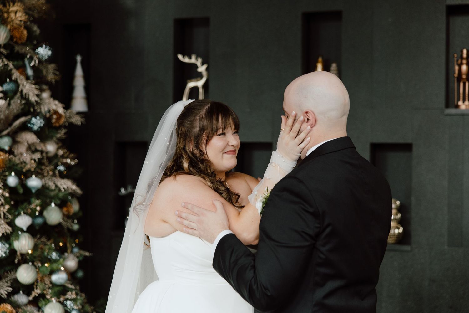 A tender moment between newlyweds during their winter wedding ceremony beside a decorated Christmas tree.