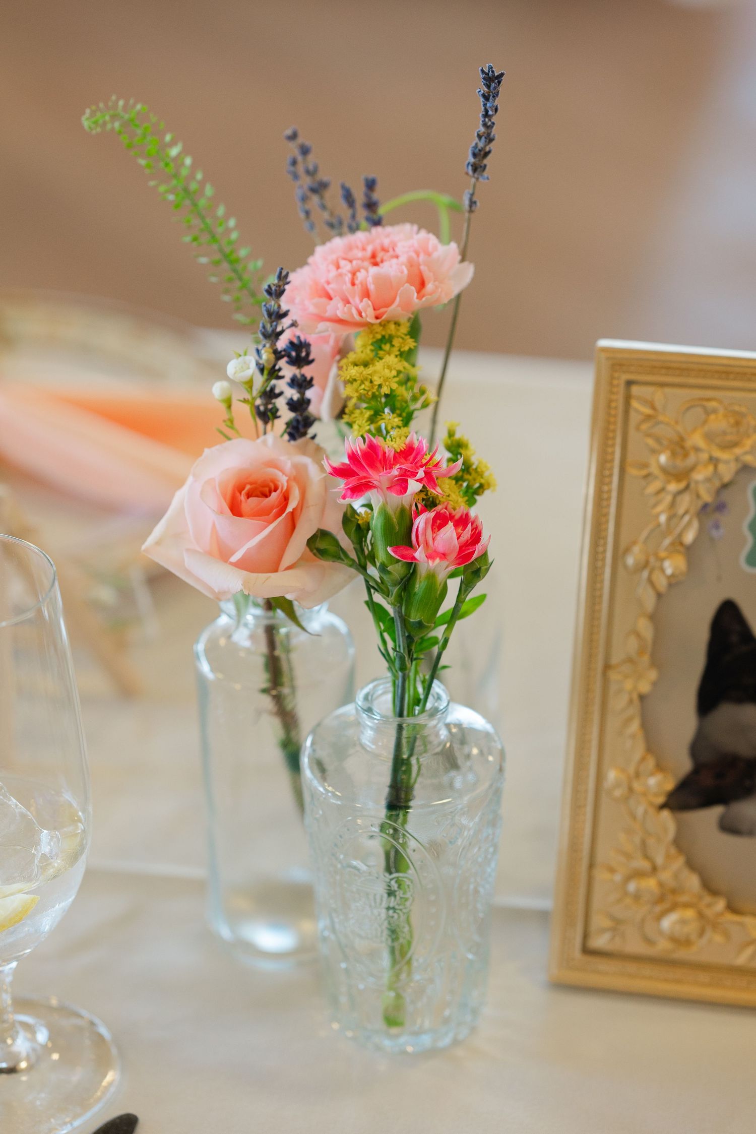 Small glass jar vases with delicate pink roses, lavender sprigs and yellow flowers create a simple floral arrangement.