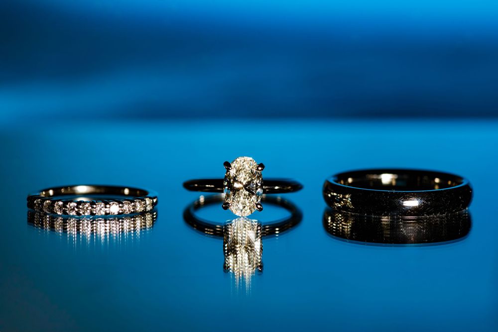 Three wedding rings displayed on reflective blue surface showing engagement ring and bands in elegant arrangement.