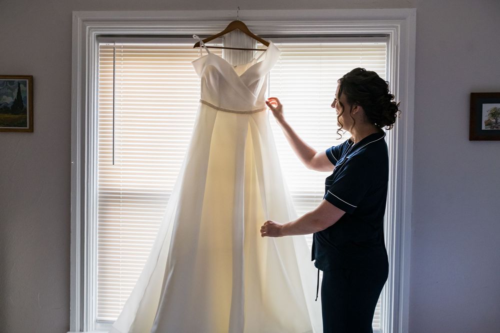 A beautiful white wedding dress hangs in front of a window while being steamed.