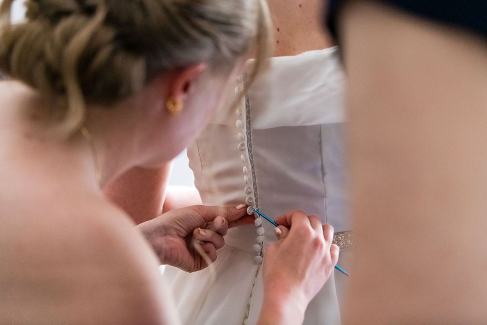 Close-up shot of delicate buttons being fastened on a white wedding dress.