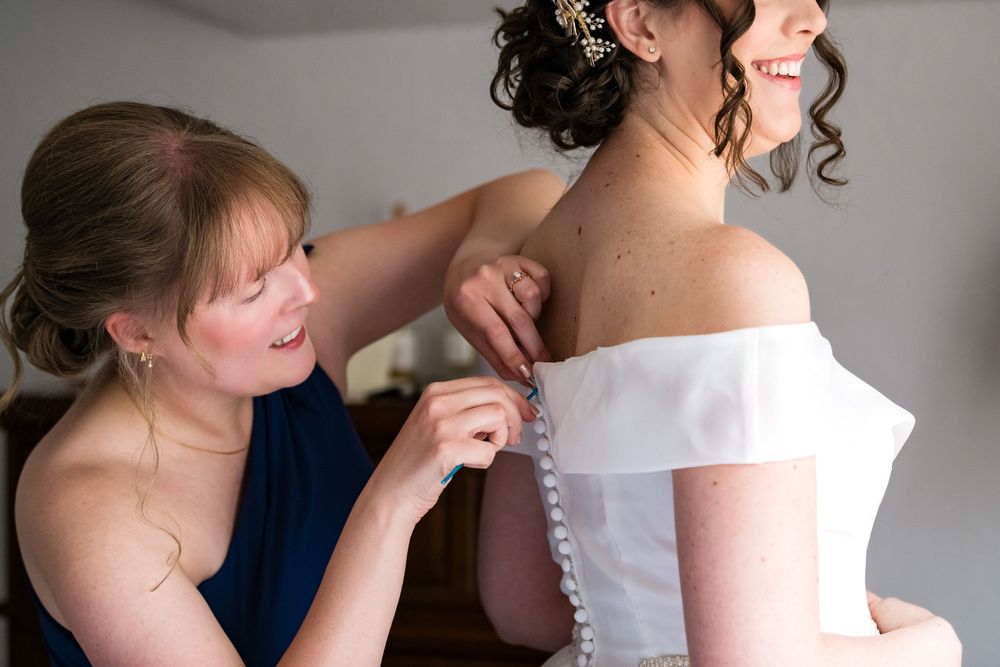A wedding dress being buttoned up during bridal preparations.