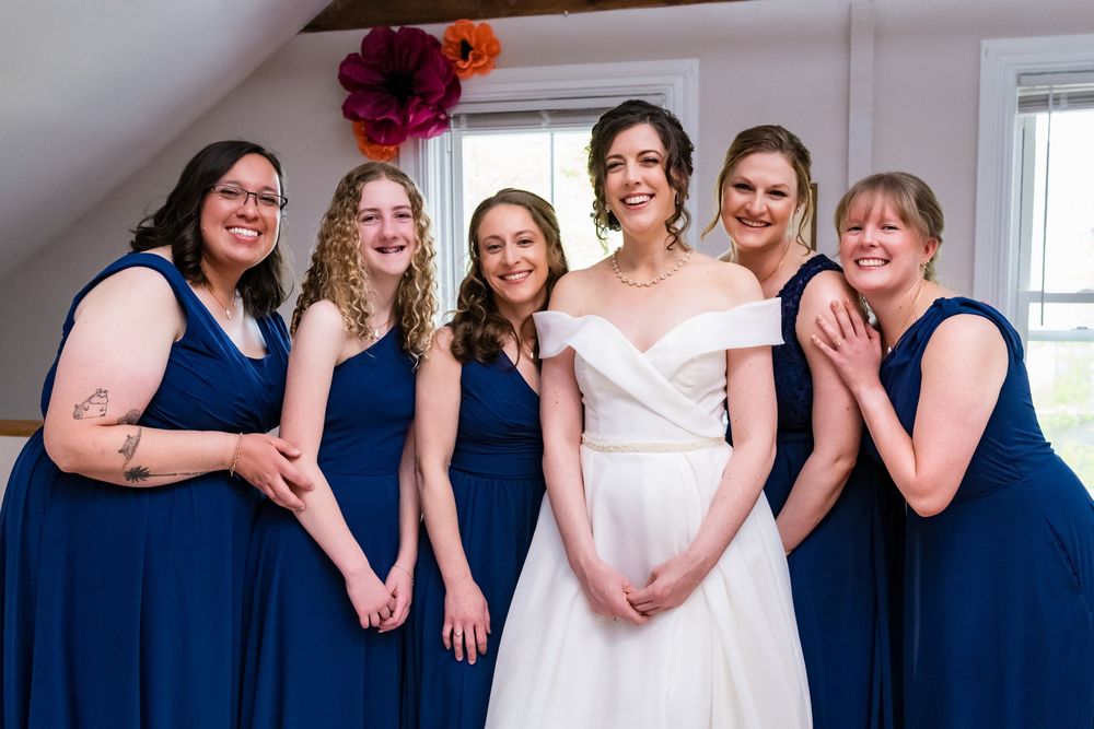 Wedding party of bridesmaids in navy blue dresses pose together with bride wearing elegant white gown.
