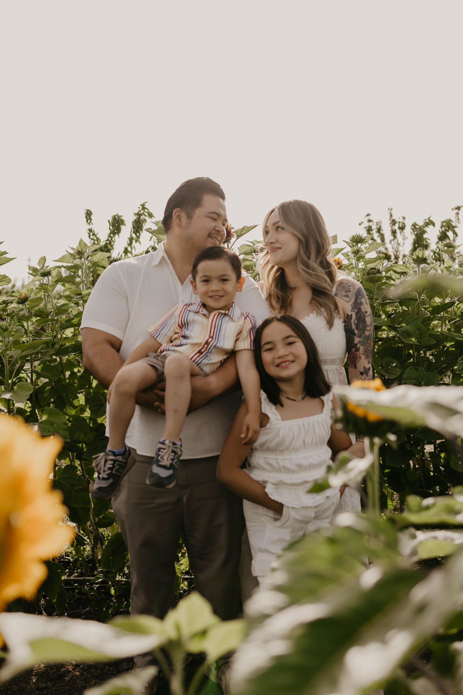 A family of four shares joyful moments together in a sunlit garden with blooming flowers and greenery.