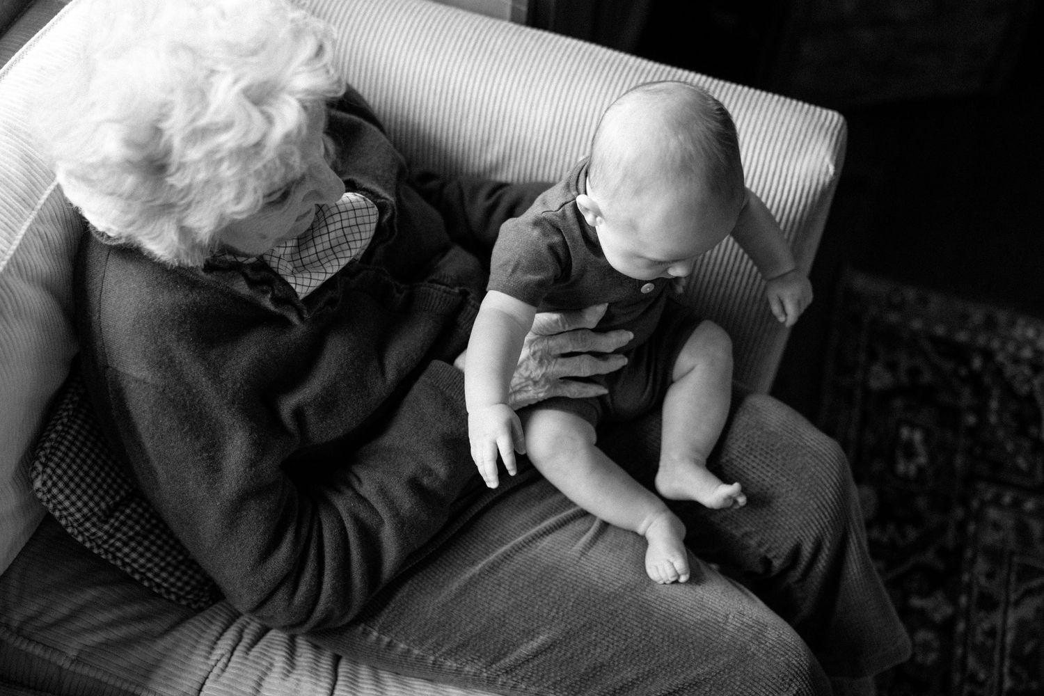 A tender moment captured in black and white showing a young baby being cradled while sitting together on a couch.