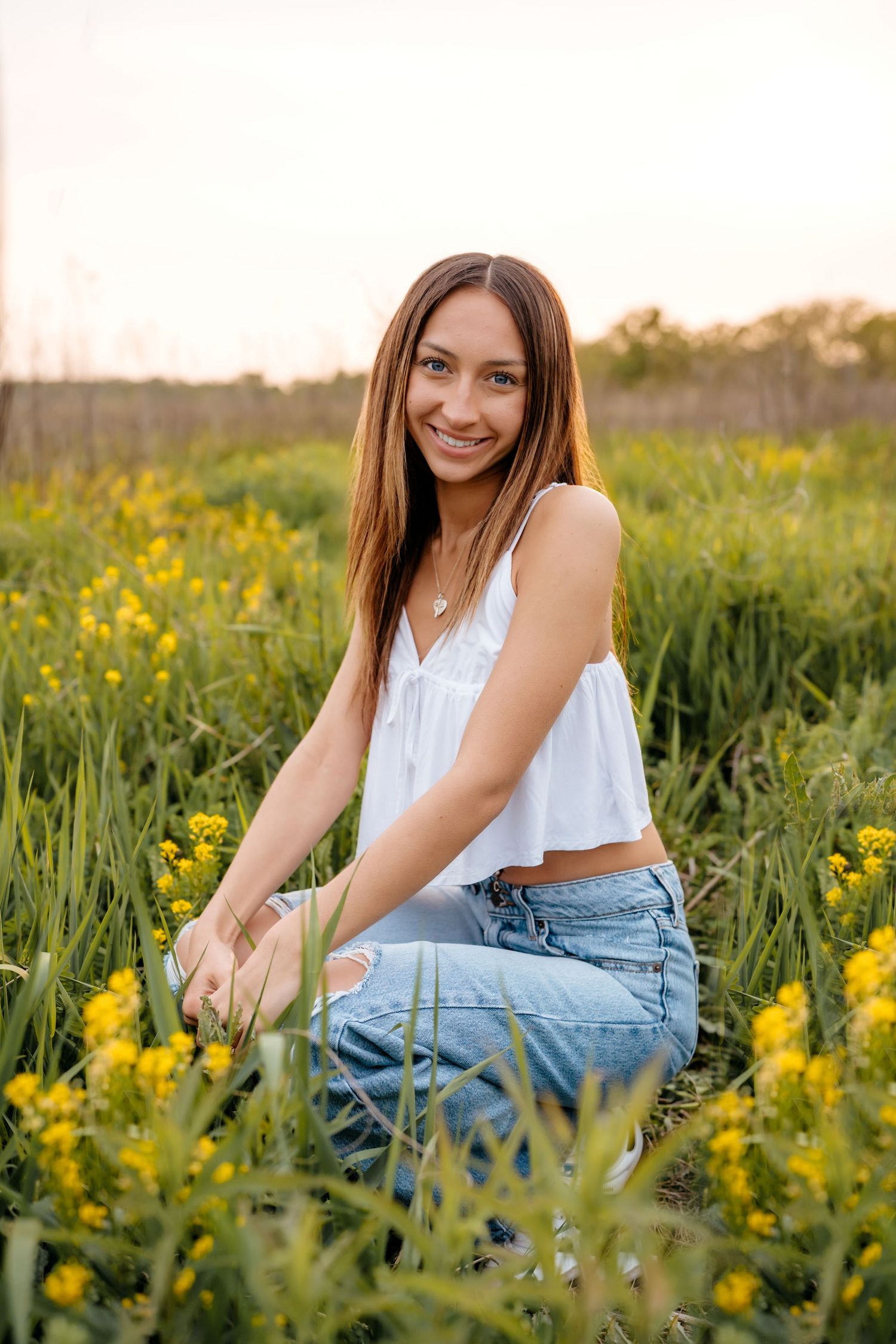 A white crop top and jeans outfit photographed in a sunny wildflower meadow filled with yellow blooms at golden hour.