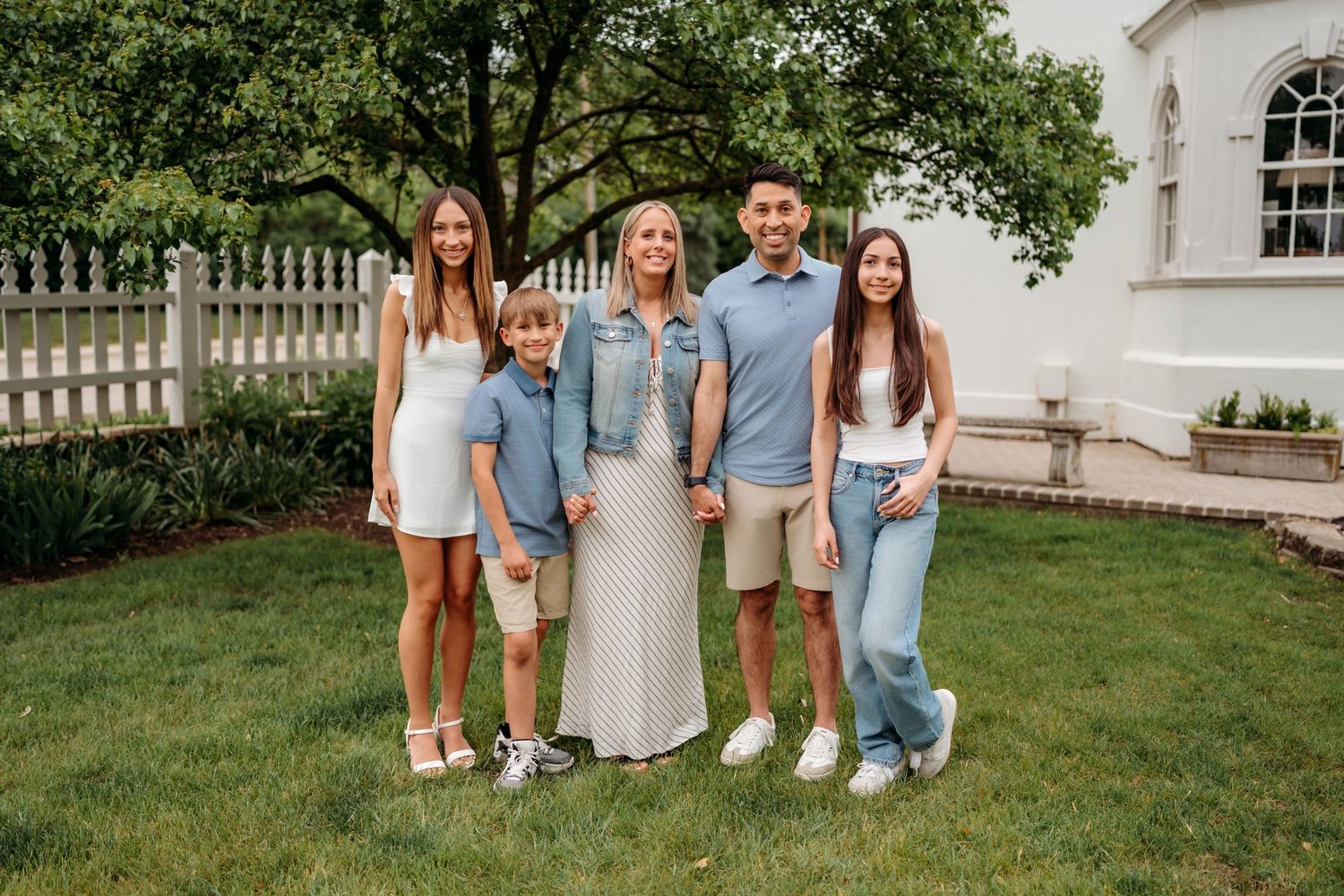 Family group in coordinated blue and white outfits poses together outdoors for casual summer photoshoot.