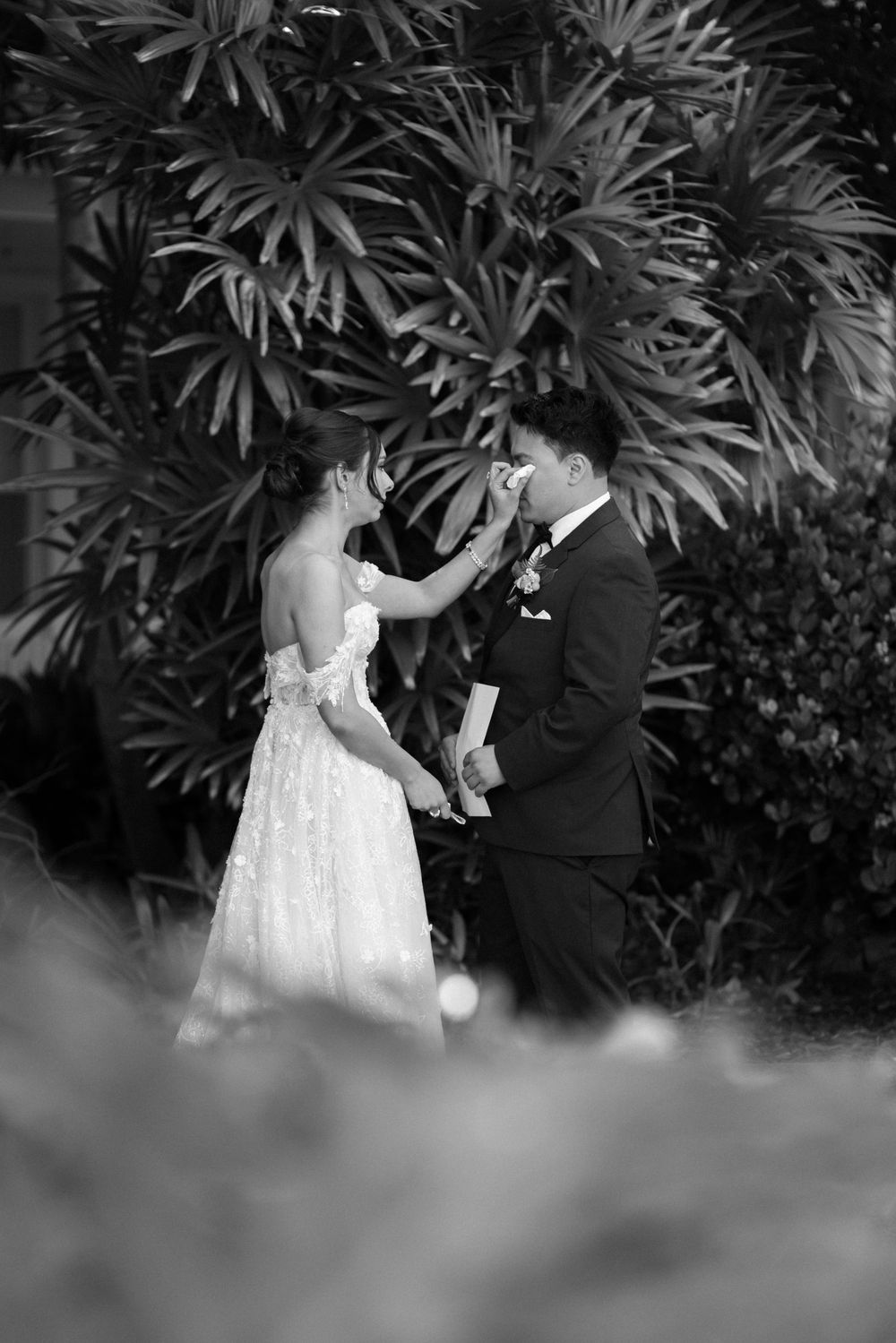A black and white intimate wedding photo captured among lush tropical foliage.