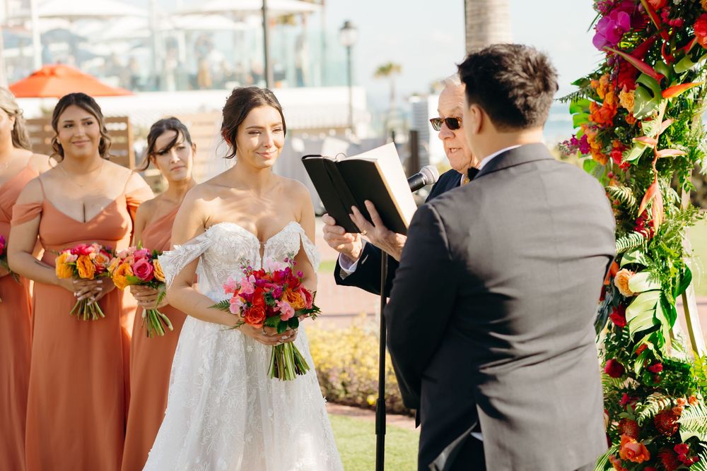 An outdoor wedding ceremony with bridesmaids in terracotta dresses and tropical floral decorations.