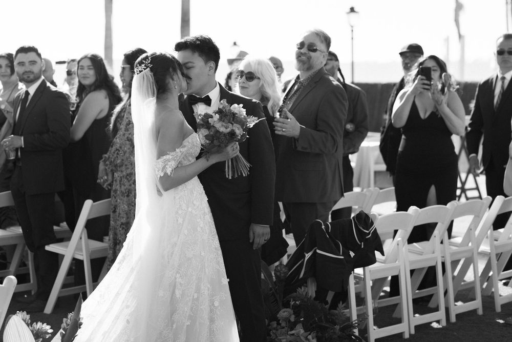 Wedding ceremony moment captured in black and white with guests looking on.