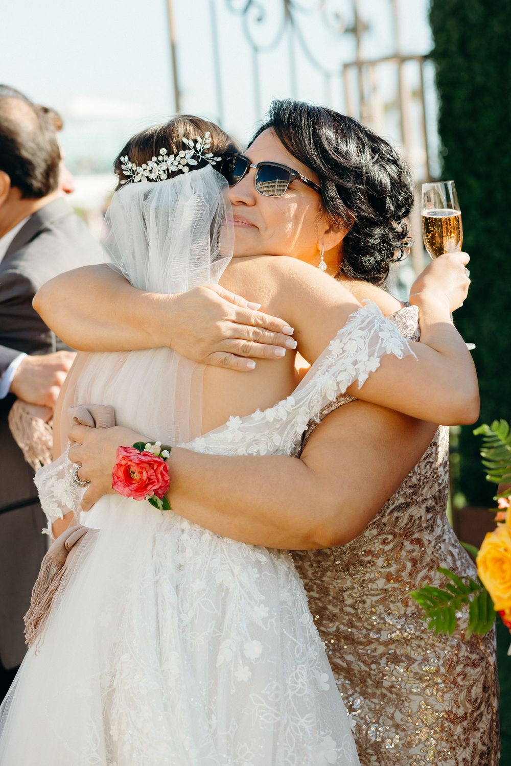Emotional embrace at wedding reception with sparkly dress details and champagne glass.