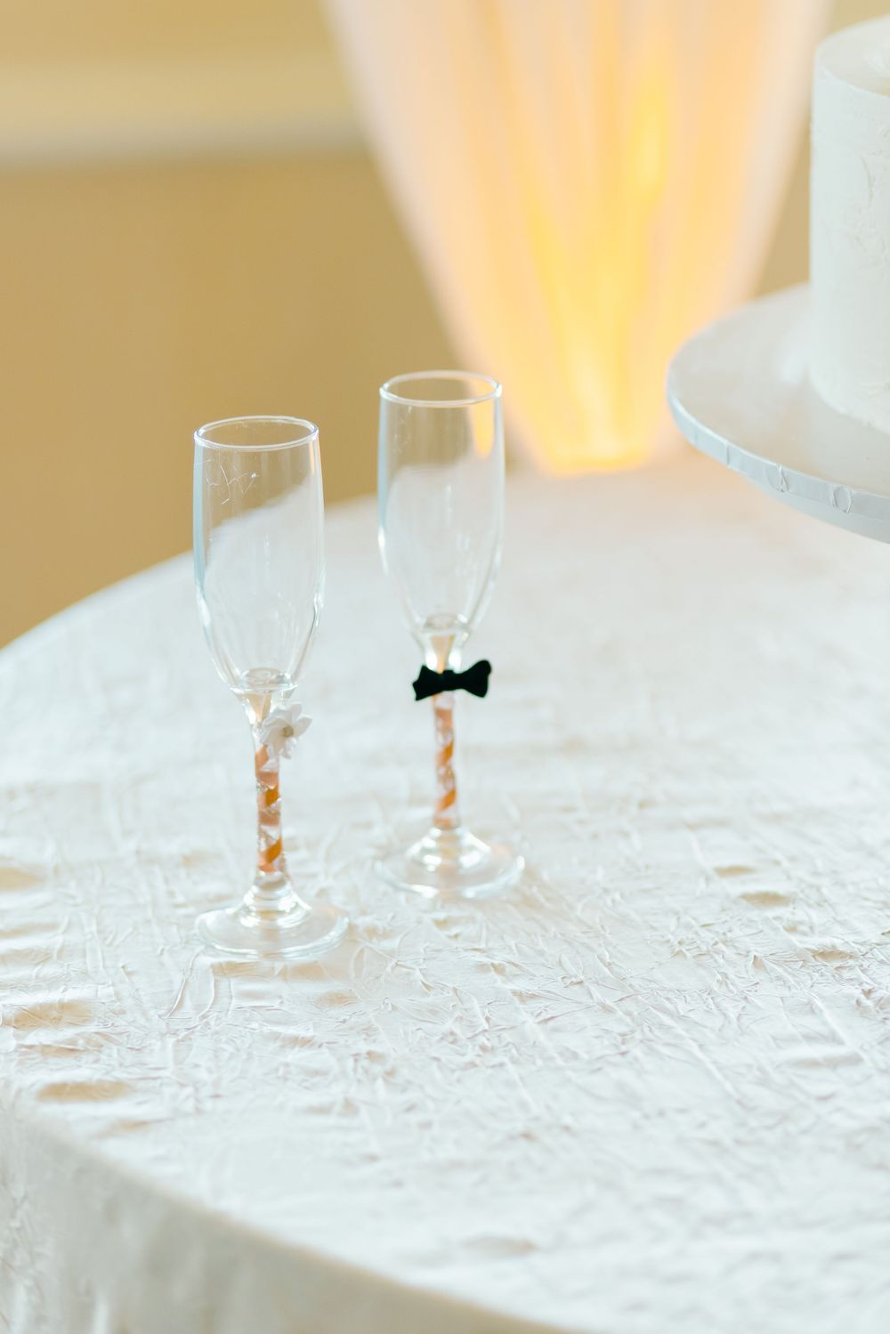 Two champagne flutes decorated with bow tie and pearl details on a white tablecloth.