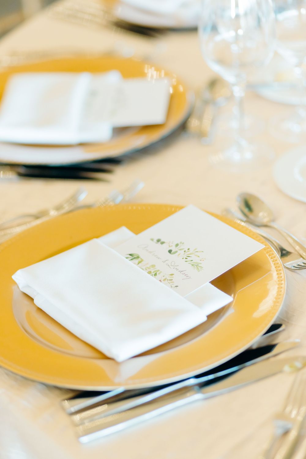 Elegant place setting with yellow charger plate, white napkin and menu card.