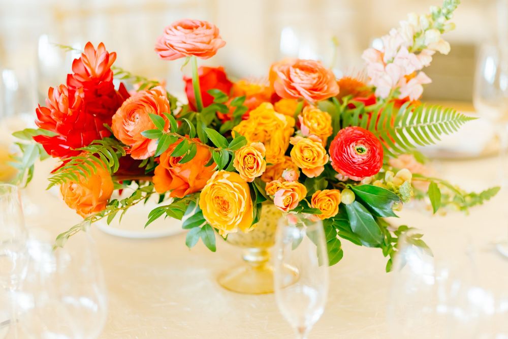 Vibrant coral and orange floral centerpiece arrangement in gold vase on wedding reception table.