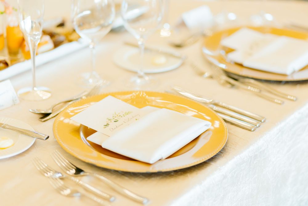 Elegant wedding table setting with white napkins and gold charger plates in a clean, minimalist style.