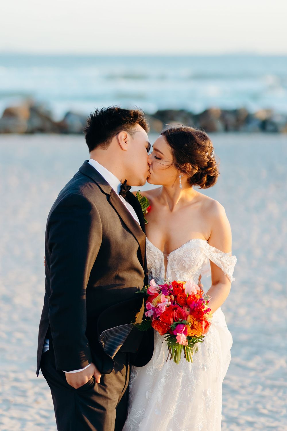 A romantic beachside moment between newlyweds with the ocean and rocks in the background.