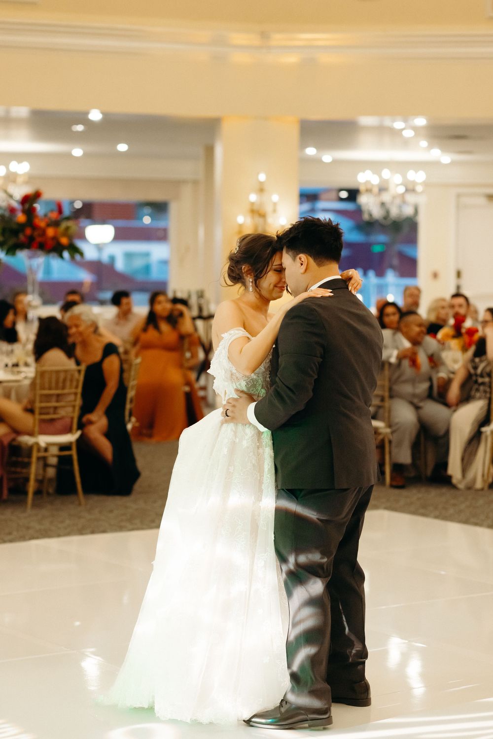 A couple shares their first dance as newlyweds on a white dance floor at an elegant wedding reception venue.