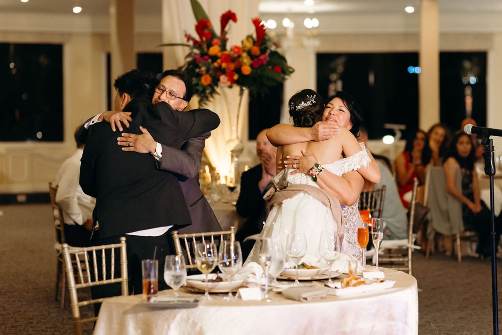 Wedding celebration moment at a reception with guests seated at decorated round tables.