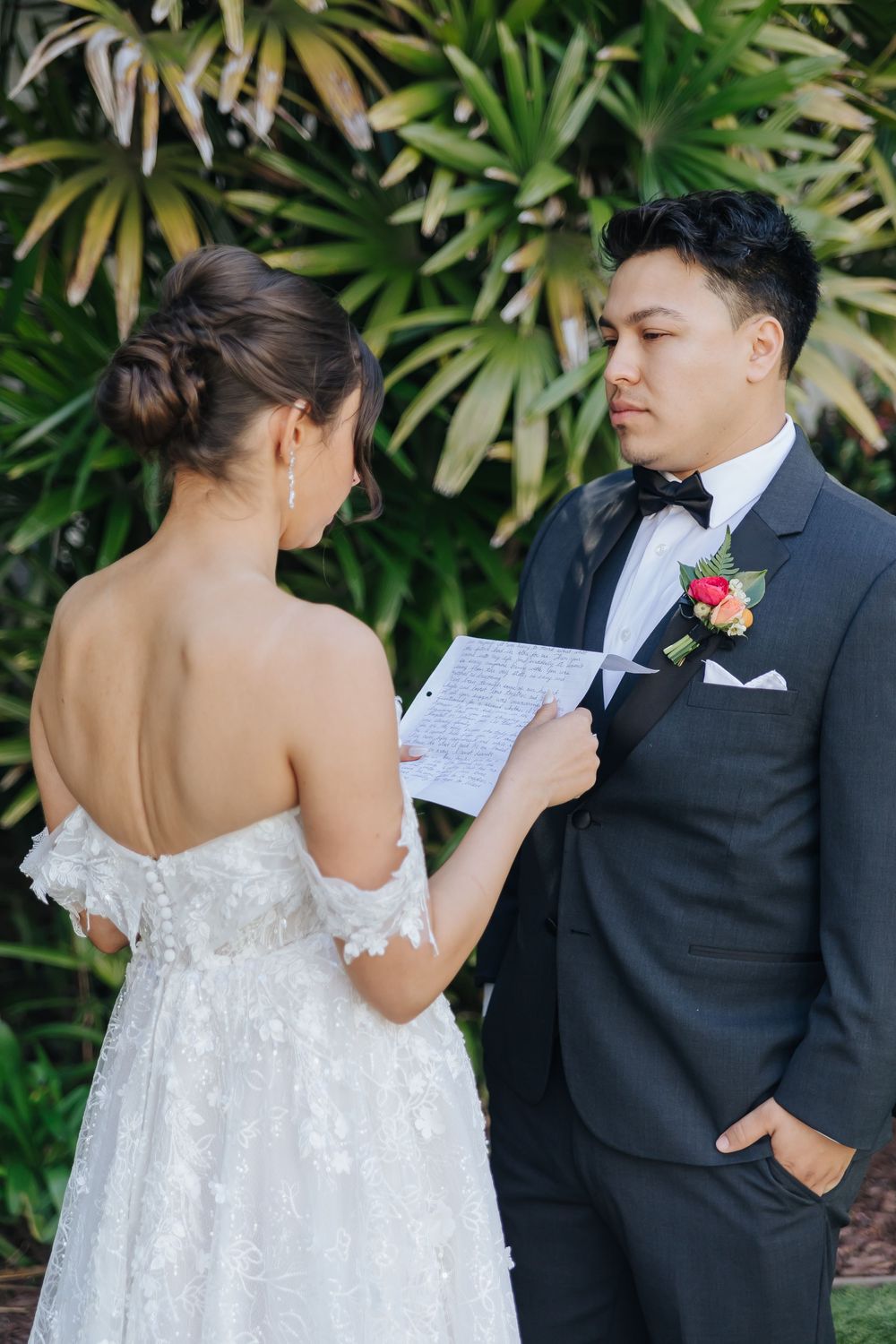 A couple shares a tender moment during their vows ceremony surrounded by tropical foliage.