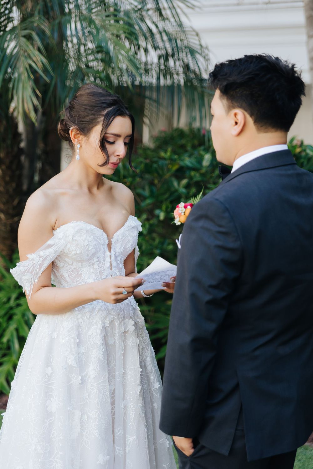 Newlyweds exchange vows in an intimate outdoor garden ceremony beneath tropical palm fronds.