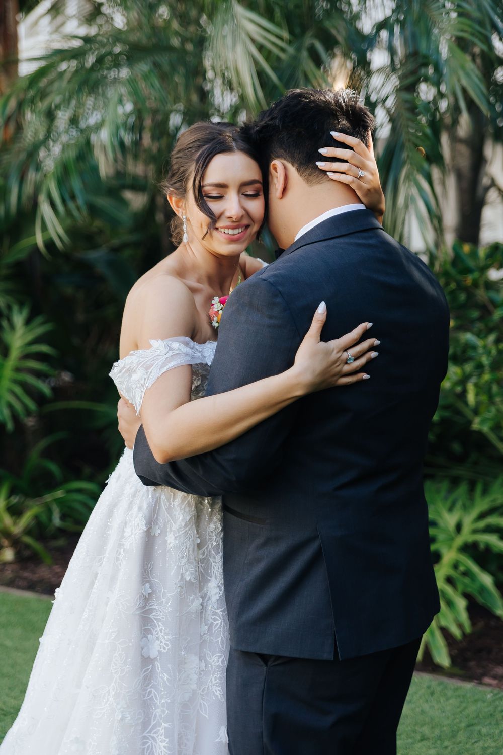 A tender embrace between wedding couple against a lush tropical garden backdrop.