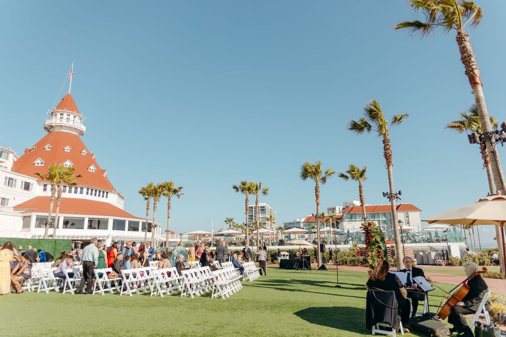 Hotel Del Coronado's iconic red turret and palm trees frame an outdoor wedding ceremony setup.