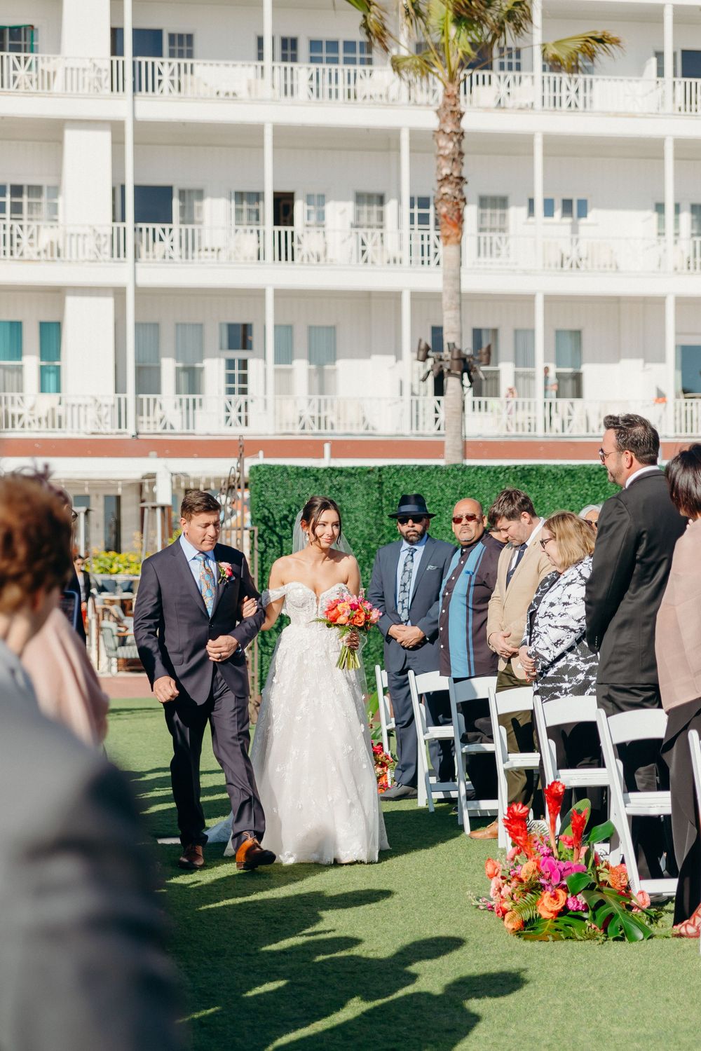 An outdoor wedding ceremony taking place on a green lawn with a white hotel building in the background.