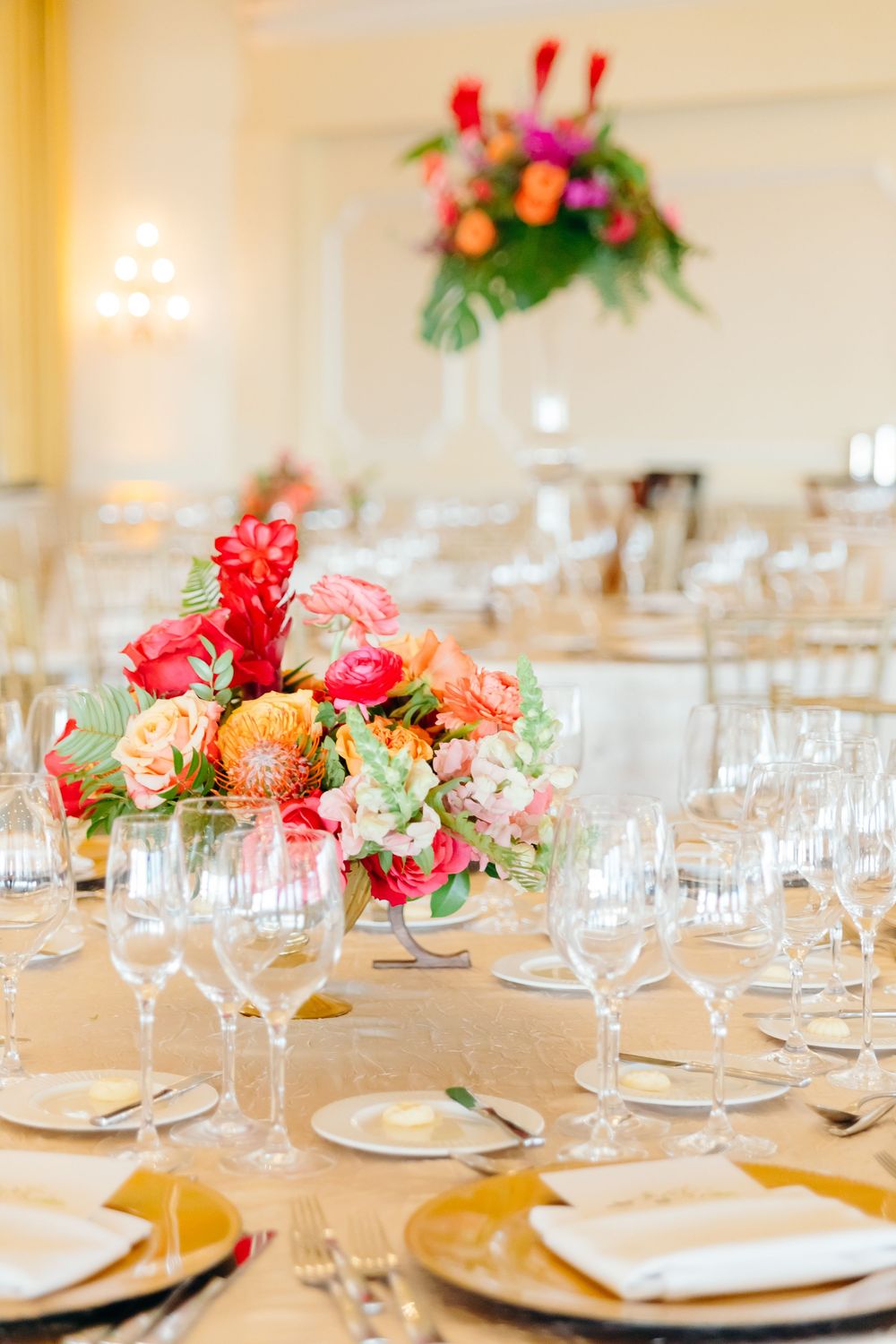 Vibrant coral and peach floral centerpiece adorns elegant table setting at reception.