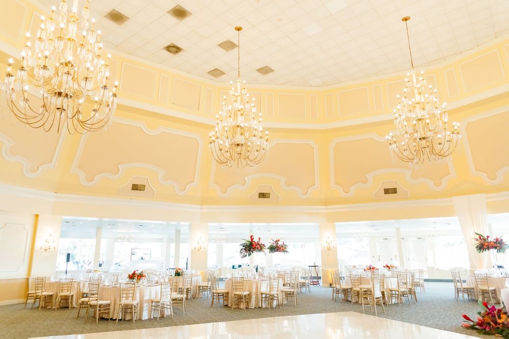 An elegant wedding reception ballroom with crystal chandeliers and yellow-tinted walls.