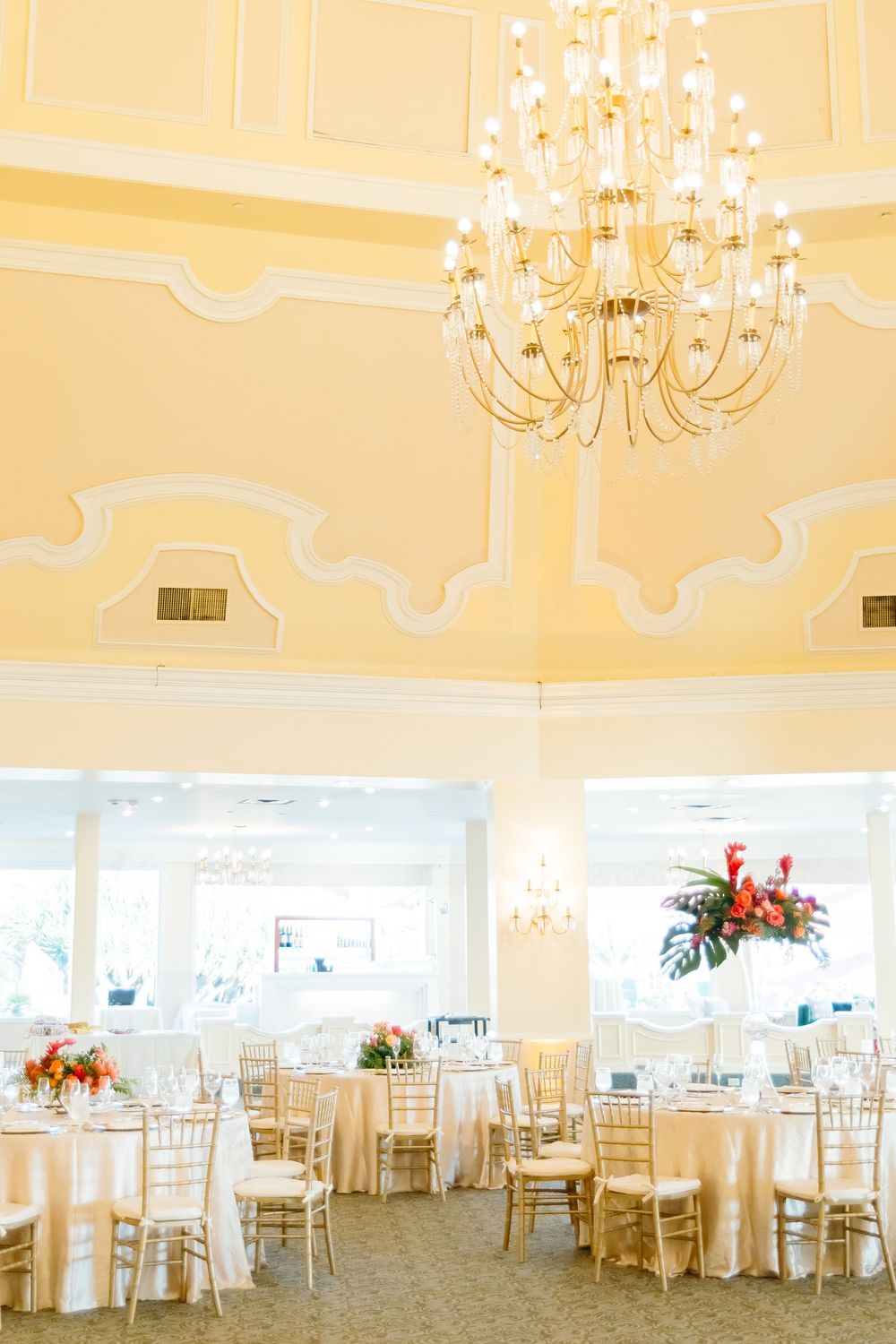 An elegant ballroom with crystal chandeliers and round tables set for a wedding reception.