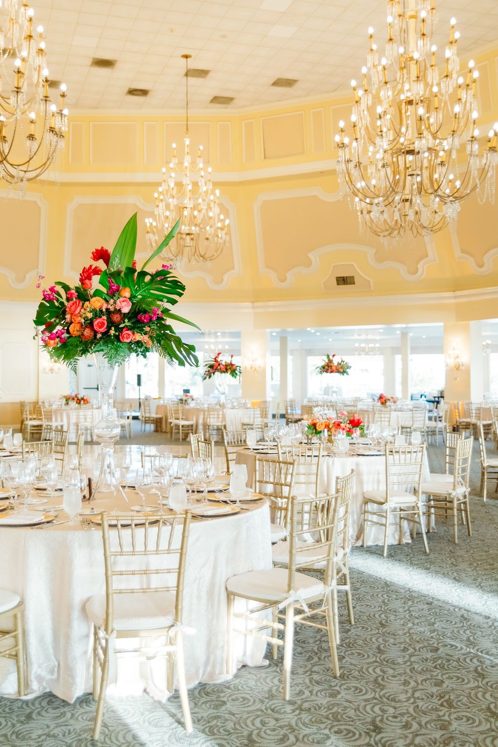 Elegant ballroom reception venue with crystal chandeliers and tropical floral centerpieces.