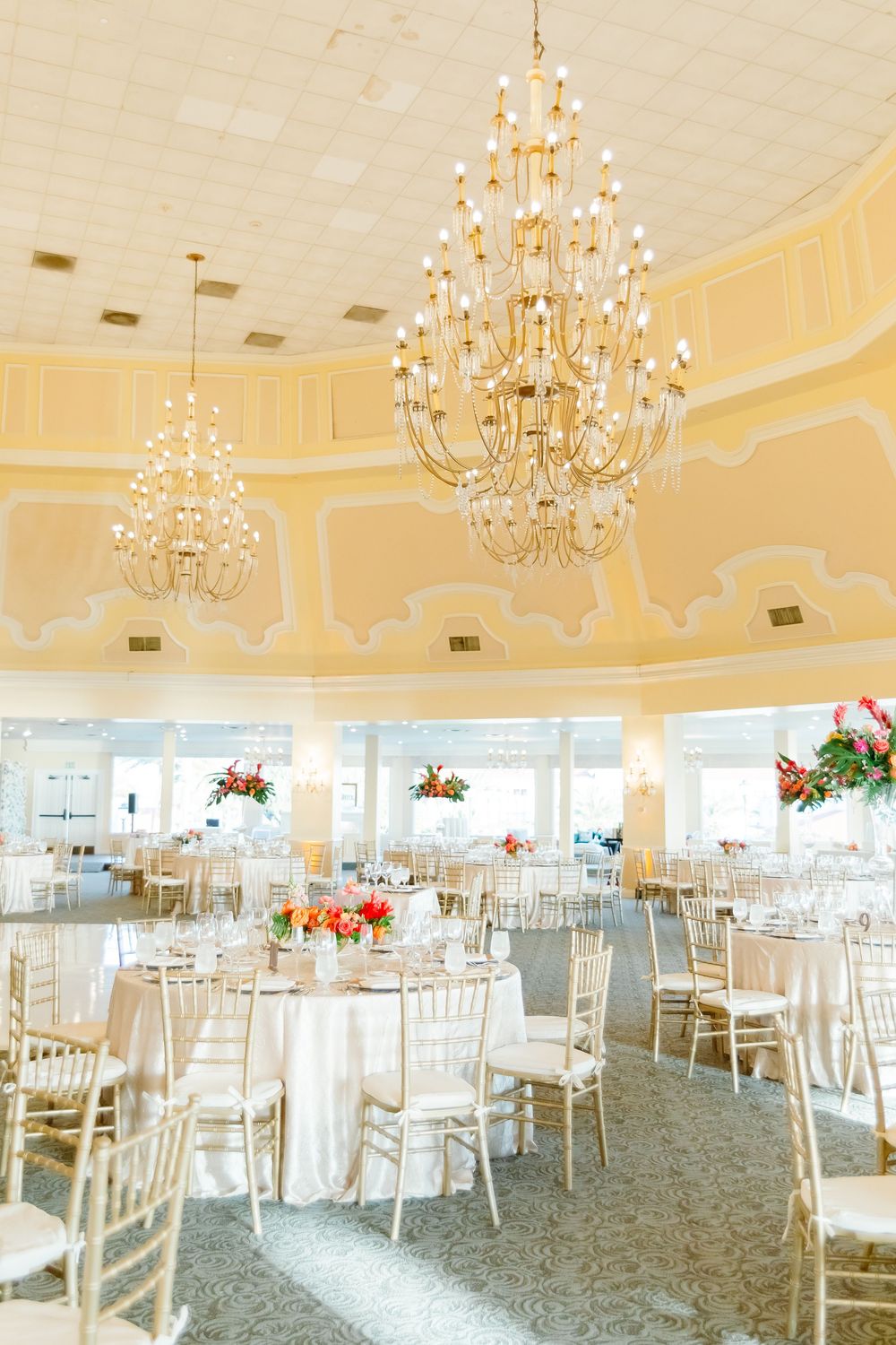 A luxurious reception venue with twin crystal chandeliers and classic white table settings.