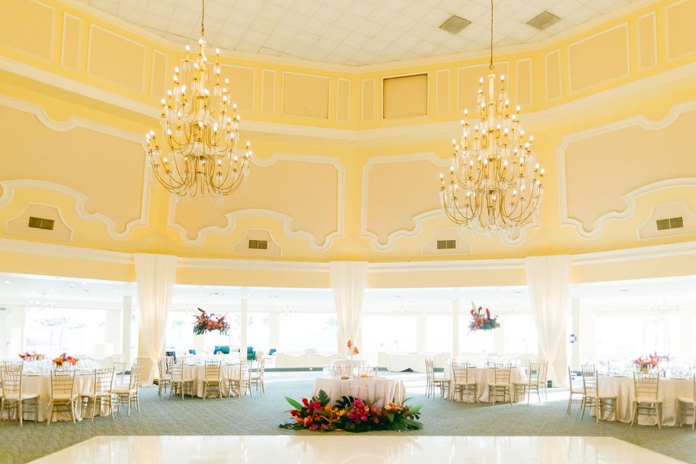 Yellow-toned ballroom with crystal chandeliers and round tables set for an elegant wedding reception.