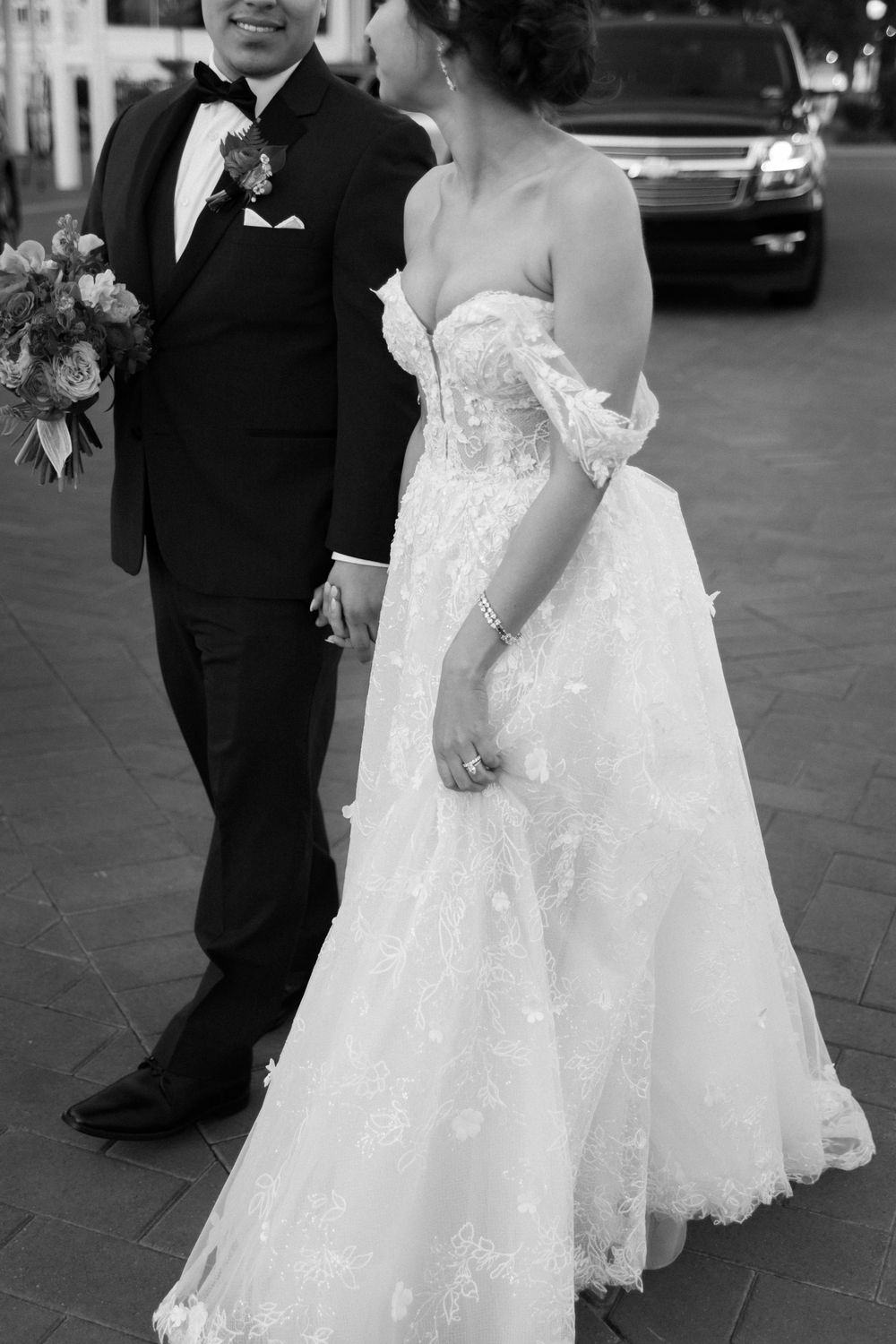 Black and white portrait showing elegant wedding attire details with lace dress and classic tuxedo.