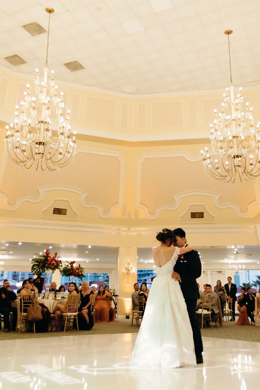 Elegant ballroom wedding reception with crystal chandeliers and couple on dance floor.