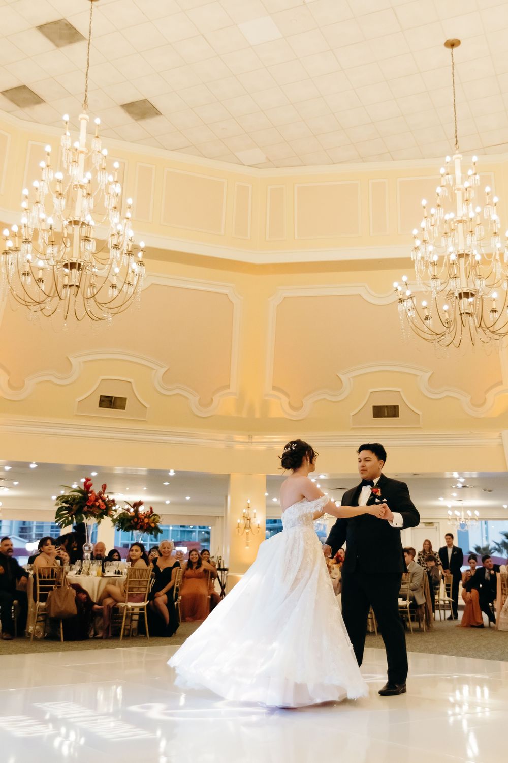Elegant ballroom with crystal chandeliers and cream walls where dancers move across a polished floor.