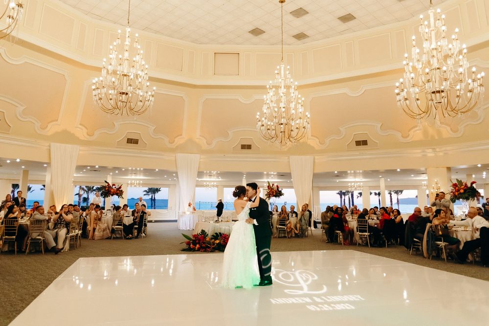 Couples first dance in grand ballroom with ornate chandeliers and circular dance floor.