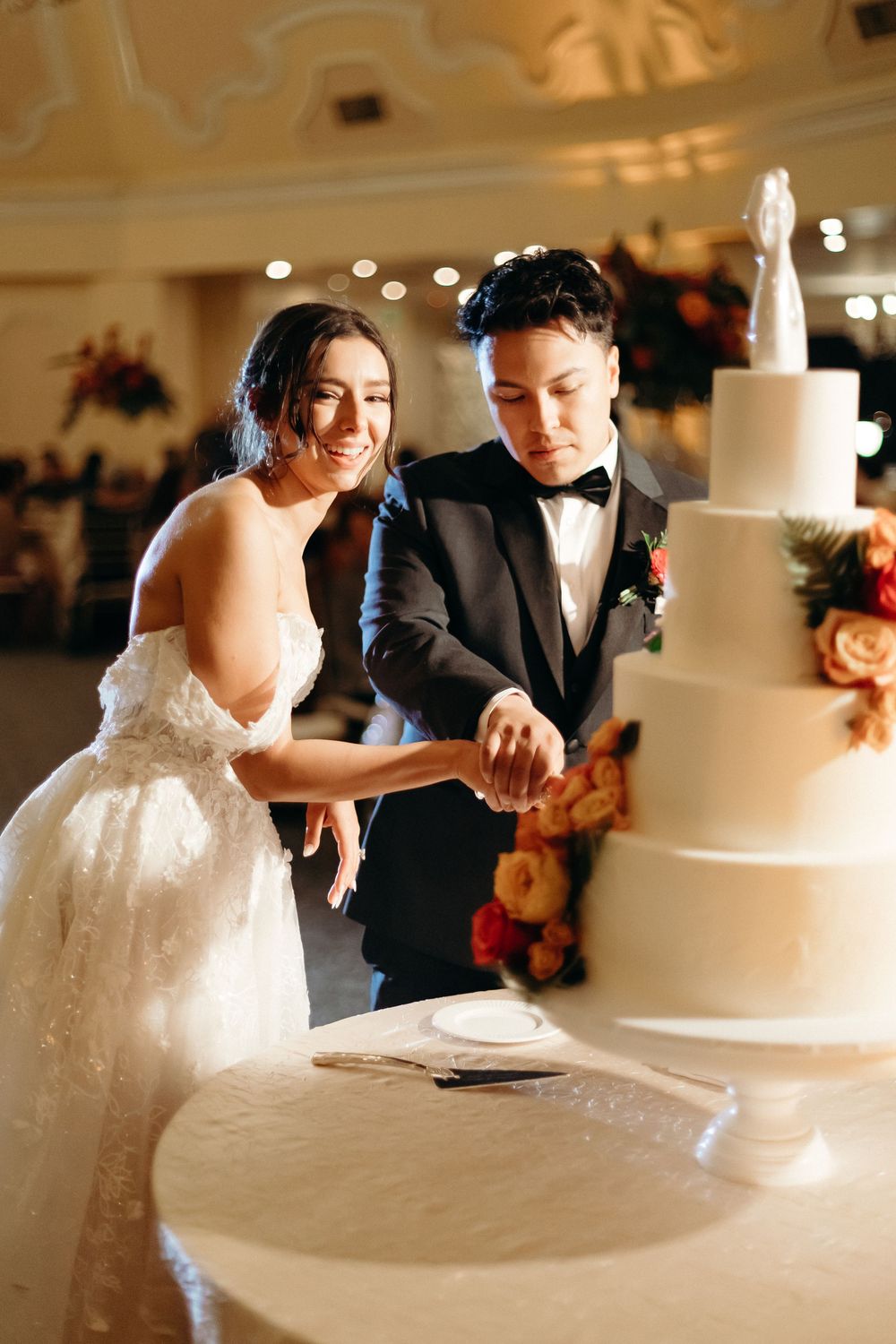 Couple shares a joyful moment while cutting their elegant white wedding cake.