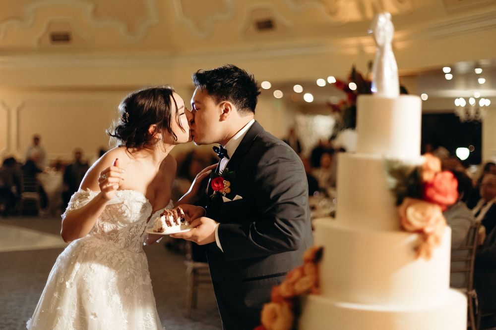 Romantic cake cutting moment in elegant ballroom with tiered white wedding cake.