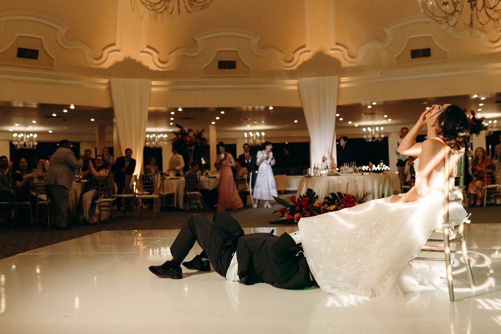 Dynamic dance move captured on a glossy ballroom floor under warm lighting and elegant chandeliers.