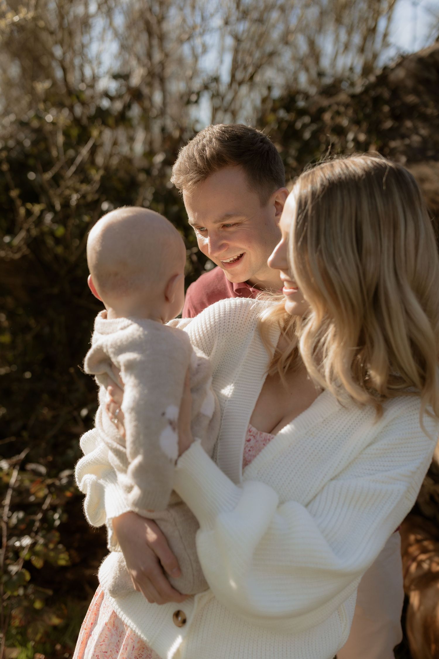 A family wearing white sweaters shares tender moments together outdoors during an autumn photoshoot.