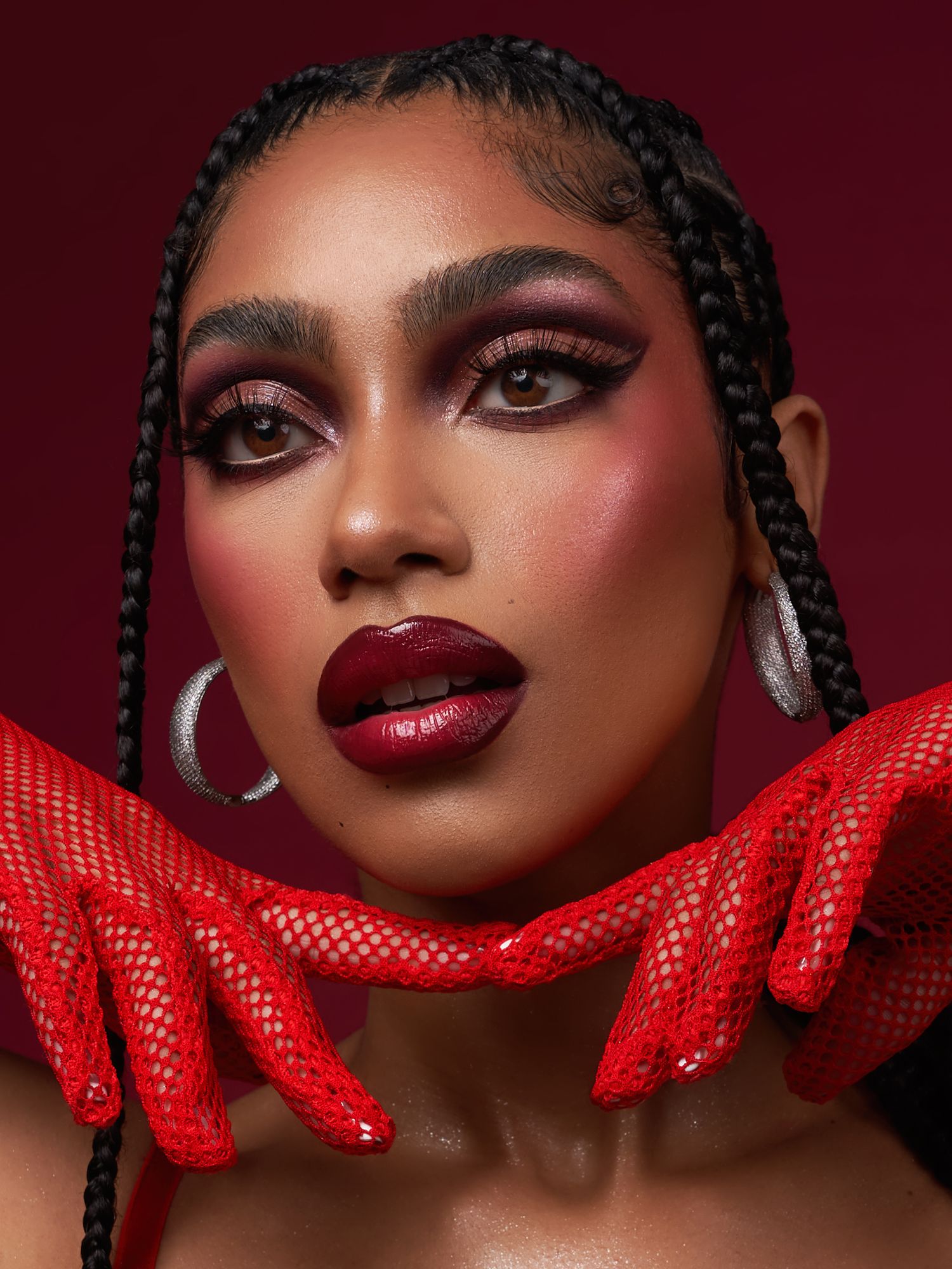Beauty portrait with burgundy lips, dramatic eye makeup and red mesh accessory against dark background.