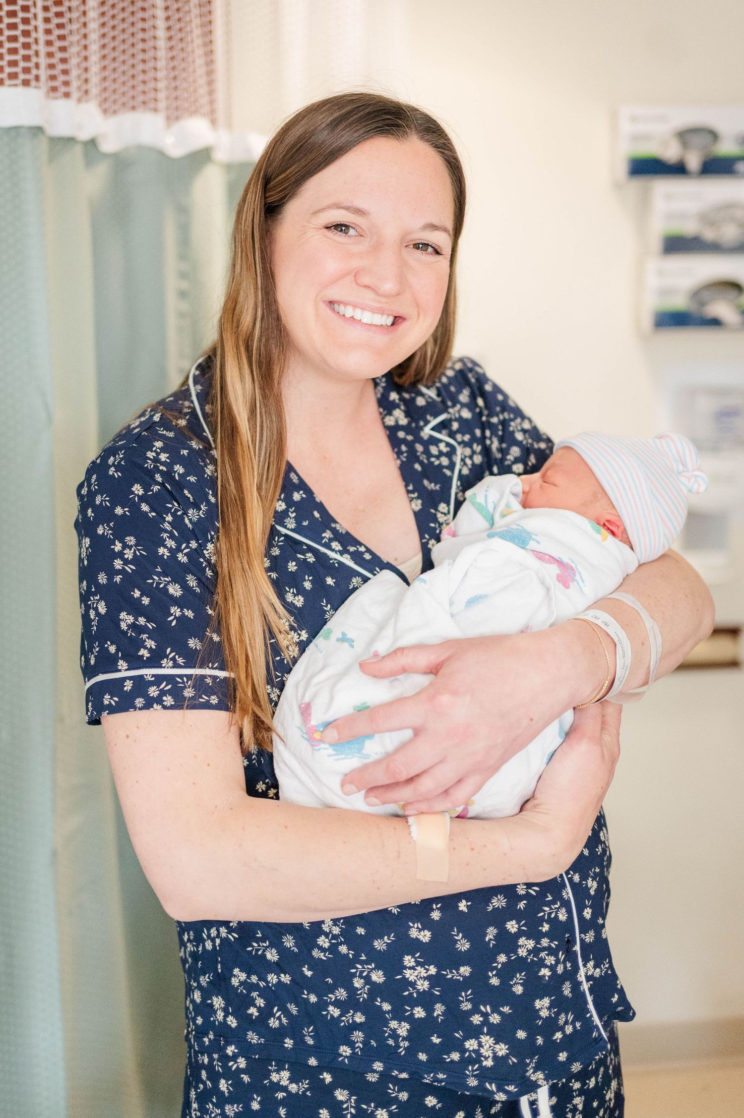Two parents hold their newborn baby in hospital room with blue floral gown and black shirt.