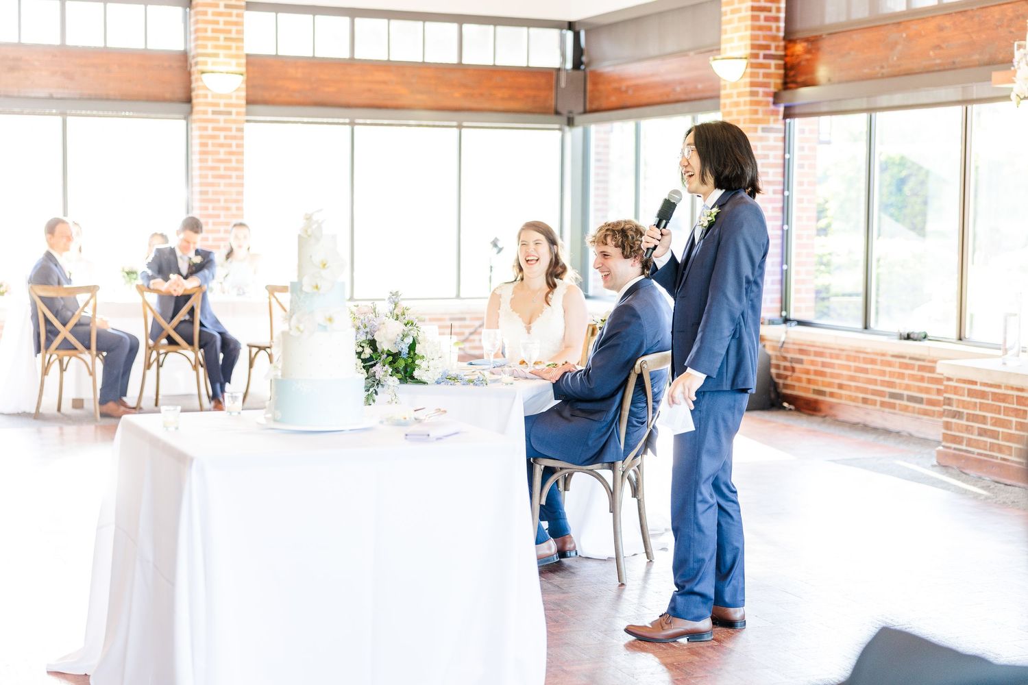 People gathered in a bright industrial event space with exposed brick walls and large windows enjoying a social occasion.